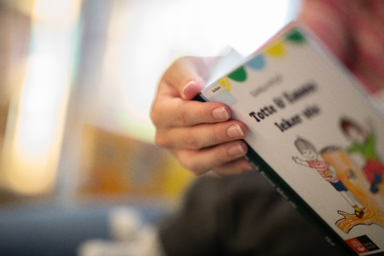 Vuxen hand håller i barnbok vid lässtund