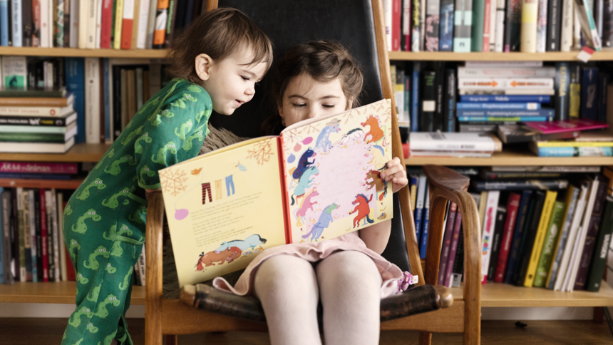 Två barn tittar i bok tillsammans i bibliotek